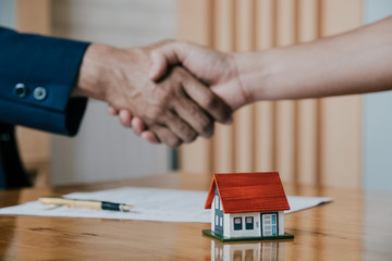 Estate agent shaking hands with his customer after contract signature, Contract document and house model on wooden desk - obrazy, fototapety, plakaty