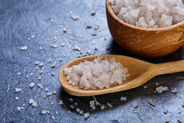 Crystal sea salt in a wooden spoon on dark background, top view, close-up, selective focus.