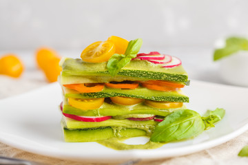 Raw vegan zucchini lasagna with vegetables and pesto sauce, light background. Vegetarian raw diet concept.