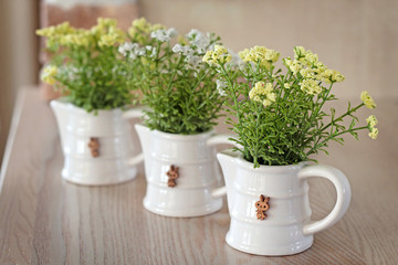 Artificial flowers in white ceramic vases on the wooden table.