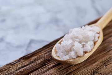 Fototapeta na wymiar Crystal sea salt in a wooden spoon on dark background, top view, close-up, selective focus.