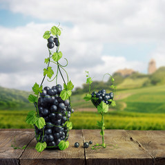 A glass and a bottle of wine made by of grape leaves and a bunch of grapes on a wooden background