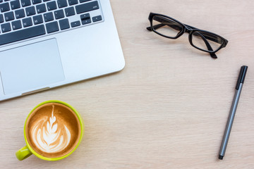 Wood office desk table with laptop, cup of coffee and supplies.Top view with copy space.