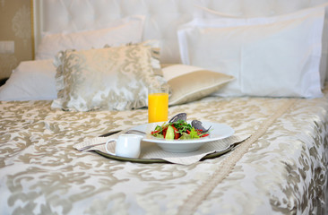Breakfast with a salad and juice in a hotel room bed.