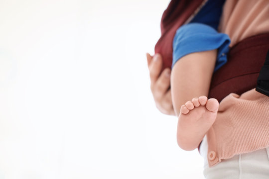 Mother with her baby in ergo carrier on light background, closeup
