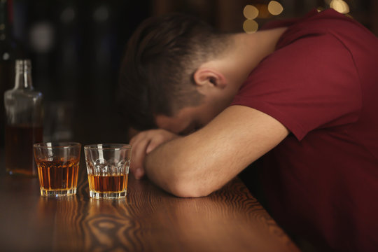 Unconscious drunk man with glasses of drink in bar. Alcoholism problem