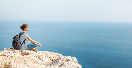 Fototapeta na wymiar A girl traveler sits on a rock and admires the blue boundless sea, freedom, travel, unity with nature,