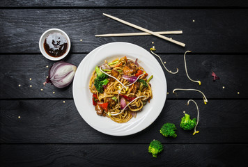 Udon stir fry noodles with meat or chicken and vegetables in a white plate with chopsticks.