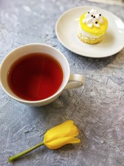yellow Tulip with a Cup of tea on a grey background with cake