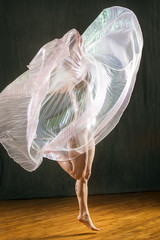 Young woman dancer turning with transparent, billowing cape.