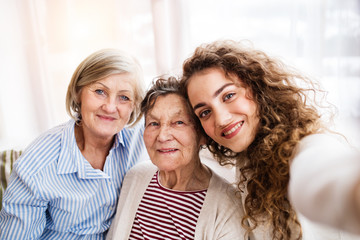 A teenage girl with mother and grandmother at home. - obrazy, fototapety, plakaty