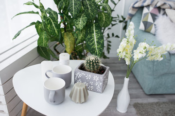 A small white coffee table with a cactus, a gray candle and cups. Interior