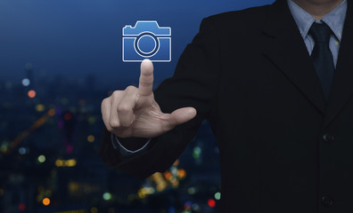 Fototapeta na wymiar Businessman pressing camera flat icon over blur colorful night light city tower, Business camera service concept