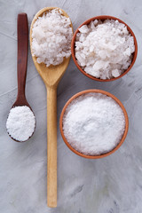 Conceptual composition of salt and pepper on spoons and bowls over light background, top view, close-up