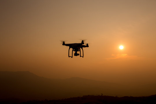 Drone silhouette flying in sunset landscape. 