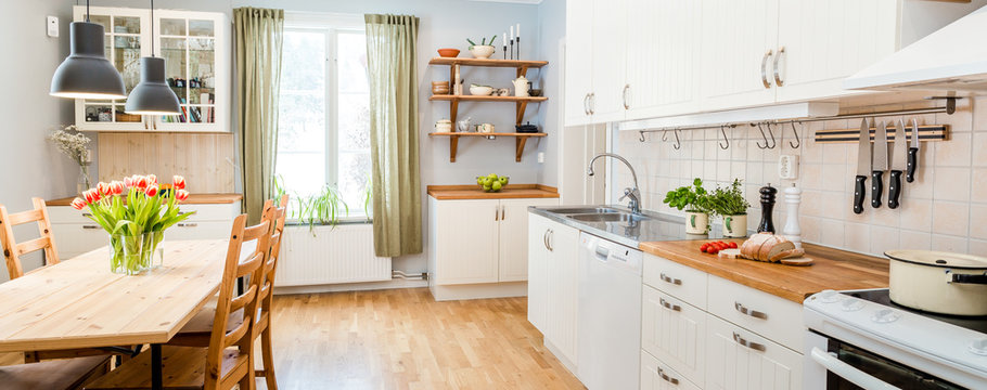 banner of a kitchen with kitchen table  and breakfast at the kitchen counter top white cupboards and wooden floor