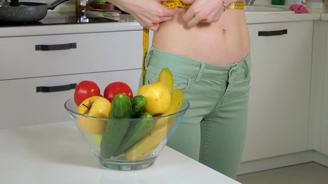 Slim woman measure waist on the background of a plate with fruits and vegetables, a healthy lifestyle