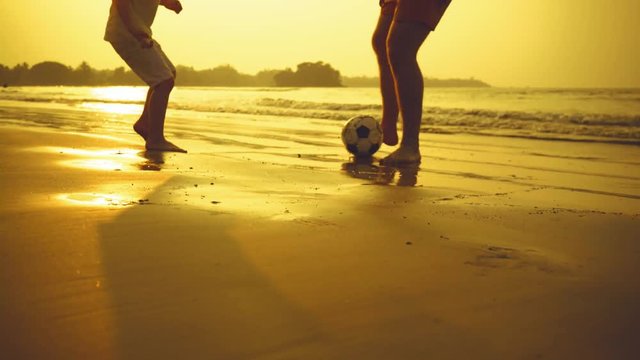 Father and son playing together with ball in football on the beach under sunset background