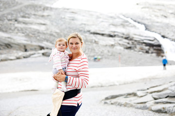 Happy mother with little baby girl travelling in backpack. Hiking adventure with child in mountains.