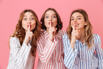 Beautiful young girls 20s wearing colorful striped pyjamas having fun and holding index fingers on...