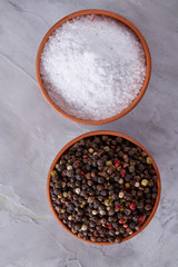 Conceptual composition of salt and pepper on spoons and bowls over light background, top view, close-up
