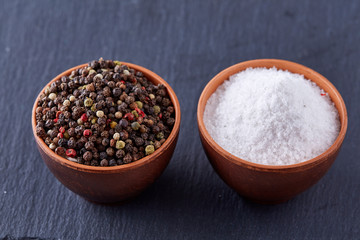 Conceptual composition of salt and pepper on spoons and bowls over dark background, top view, close-up