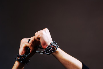 Close-up shot of male hands wound by chain. Slave concept. Iron chain. Chained hand.
