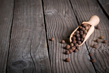 Pepper peas in a wooden spoon on a wooden background. Spices are scattered on the table