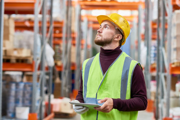 Waist up portrait of modern warehouse worker using digital tablet looking up at tall shelves, copy space