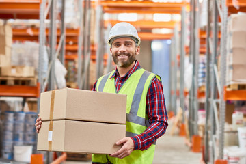 Waist up portrait of mature warehouse worker holding cardboard box smiling happily and looking at...