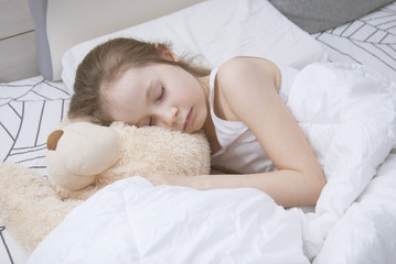 Obraz na płótnie Canvas Beautiful 7-8 year Old Girl Sleeping Girl in the Bedwith Teddy Bear with Copy Space. Flat Lay.