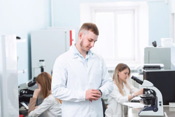 Naklejka na ściany i meble Working in the lab, portrait of handsome young scientist man posing in his laboratory with people on background. Chemistry biology medical concept