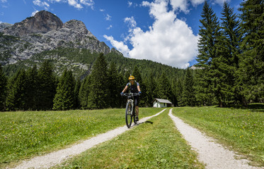 Fototapeta premium Tourist cycling in Cortina d'Ampezzo, stunning rocky mountains on the background. Woman riding MTB enduro flow trail. South Tyrol province of Italy, Dolomites.