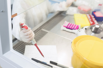 Young female scientist working in sterile genetics laboratory with pipette in white medical...