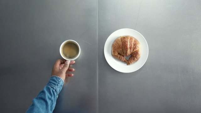 breakfast with coffe and croisant top view how man's hand put on table dish with croissant and cup of coffe