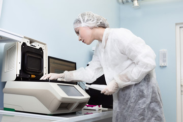 Female genetics worker placing the strips with DNA into the PCR thermal cycler or amplifier for PCR...