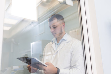 Close-up of male doctor constitutes an anamnesis or filling medical form behind the glass door