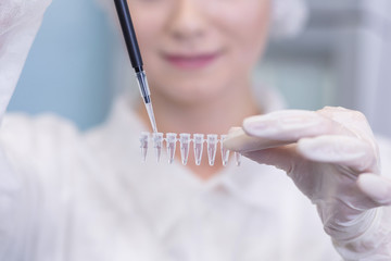 Close-up of female technician with multipipette and in genetic laboratory doing PCR research. Young woman is genetics scientist and she loads saliva samples for DNA amplification