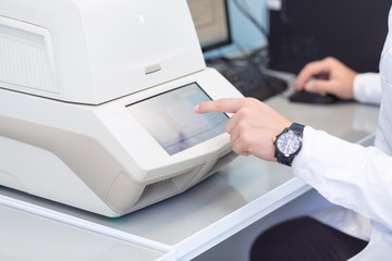 Female genetics worker placing the strips with DNA into the PCR thermal cycler or amplifier for PCR diagnostics