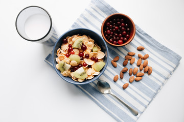 Delicious crispy cornflakes with kiwi pieces and cranberries in bowl, almonds on dish cloth, closeup, healthy breakfast