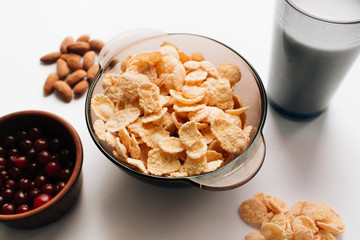 Delicious crispy cornflakes in bowl, cranberries and almonds on white background, healthy breakfast