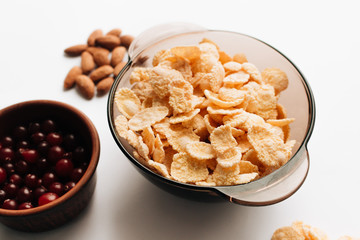 Delicious crispy cornflakes in bowl, cranberries and almonds on white background, healthy breakfast