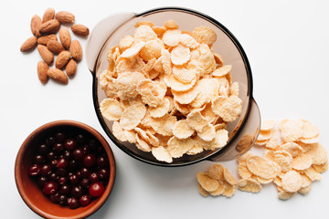 Delicious crispy cornflakes in bowl, cranberries and almonds on white background, healthy breakfast
