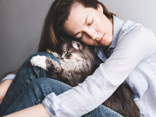Stylish, young woman gently hugging her kitten on a white background. People, pets, care	