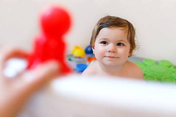 Cute adorable baby girl taking foamy bath in bathtub. Toddler playing with bath rubber toys.