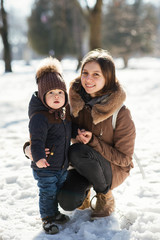 Mother holds hand of a charming little boy standing on the sparkling snow in park