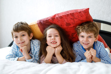 Three happy kids in pajamas celebrating pajama party. Preschool and school boys and girl having fun...