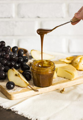 Honey flows from spoon into jar on wooden Board with homemade cheese and fruits