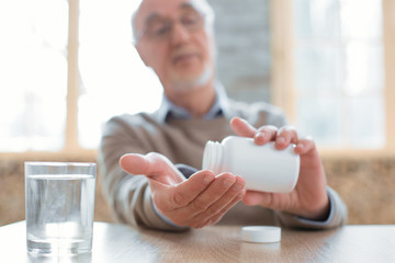 Prescribed medication. Selective focus of senior male hands holding bottle while man putting pills...