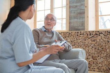 My complaints. Doctor holding clipboard while taking notes and talking to experienced smart senior man